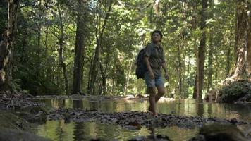 una excursionista con mochila toma una foto con un teléfono móvil en un bosque tropical mientras se encuentra entre un pequeño arroyo. video