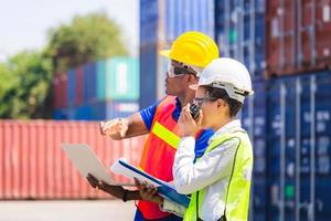 Worker man in hardhat and safety vest holding laptop and Female foreman talks on two-way radio control loading containers box from cargo photo