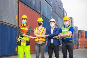 trabajador de fábrica y equipo de ingenieros con mascarilla de protección, equipo tomándose de la mano y parados en fila en contenedores de carga foto