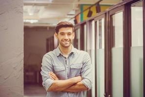 Cheerful young business man standing with arms crossed in office photo