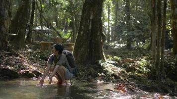 Female tourist with backpack washing hands in water stream in tropical forest. video