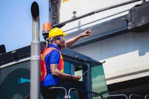 Worker man in hardhat and safety vest holding laptop standing on container stackers control loading containers box from cargo photo