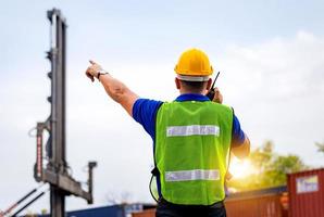 Foreman in hardhat and safety vest talks on two-way radio control loading containers box from cargo photo