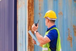 Foreman in hardhat and safety vest talks on two-way radio control loading containers box from cargo photo