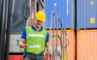 Worker man in hardhat and safety vest standing on container stackers control loading containers box from cargo photo