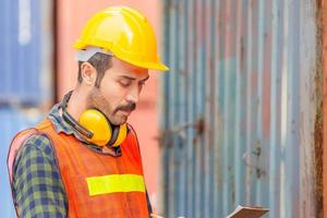 retrato de un trabajador de fábrica con casco y chaleco de seguridad, ingeniero con fondo de caja de contenedores en la carga foto