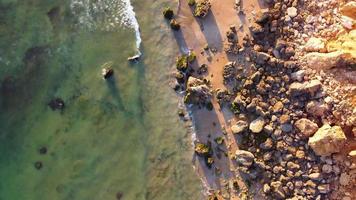 incredibile vista aerea panoramica del drone della spiaggia e dell'oceano con onde calme durante un tramonto con colori vivaci. algarve, portogallo. acque limpide. ferie e ferie. sfondo. spiaggia con scogli. video