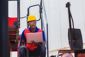 Worker man in hardhat and safety vest holding laptop standing on container stackers control loading containers box from cargo photo