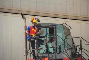 Worker man in hardhat and safety vest holding laptop standing on container stackers control loading containers box from cargo photo