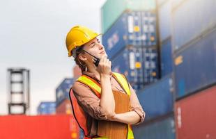 Engineer in hardhat and safety vest holding clipboard checklist and two-way radio at containers cargo photo