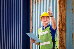 Foreman worker in hard hat and safety vest smiling and pointing control loading containers box from cargo photo