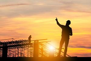 Silhouette of Engineer man with clipping path and worker on building site, construction site at sunset in evening time photo