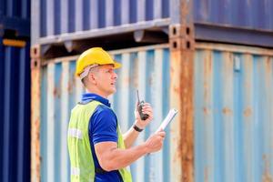 Foreman worker in hardhat and safety vest talks on two-way radio control loading containers box from cargo photo