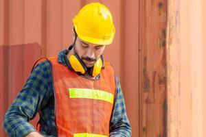 trabajador de fábrica con casco y chaleco de seguridad en contenedores de carga foto