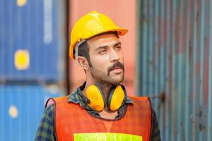 retrato de un trabajador de fábrica con casco y chaleco de seguridad, ingeniero con fondo de caja de contenedores en la carga foto