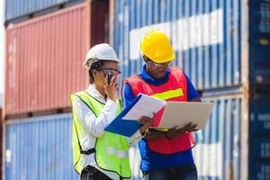 Female foreman safety vest using clipboard checklist and Worker man in hardhat holding laptop for control loading containers box from cargo photo