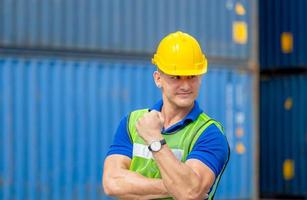 Happiness foreman worker in hardhat show strong arm muscles at containers cargo on a hot day