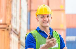 Happiness foreman in hardhat and safety vest talks on two-way radio control loading containers box from cargo photo