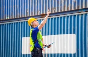 Factory worker man in hard hat holding clipboard checklist and pointing to the sky at container cargo photo