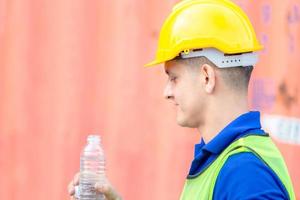 Close up of Worker man in hard hat drinking water at containers cargo photo