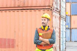 Cheerful factory worker man in hard hat smiling with arms crossed and holding clipboard checklist photo