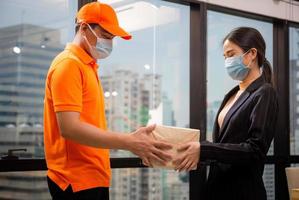 Woman wear face mask receiving parcel from delivery service, Young delivery man employee in t-shirt uniform wear face mask photo