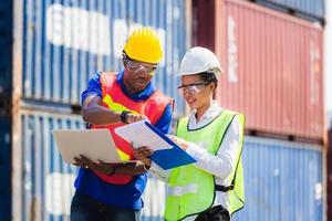 Female foreman safety vest using clipboard checklist and Worker man in hardhat holding laptop for control loading containers box from cargo photo