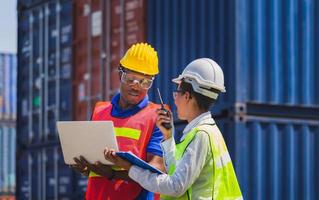 Worker man in hardhat and safety vest holding laptop and Female foreman talks on two-way radio control loading containers box from cargo photo