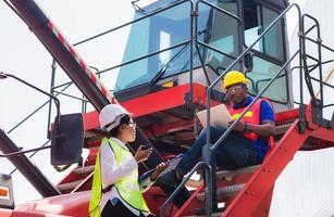 Female foreman safety vest using clipboard checklist and Worker man in hardhat holding laptop for control loading containers box from cargo photo