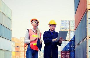 Female foreman safety vest using clipboard checklist and Worker man in hardhat holding laptop for control loading containers box from cargo photo