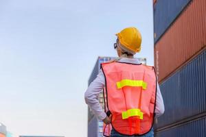 Rear view cheerful female foreman worker in hard hat looking and control loading containers box from cargo photo