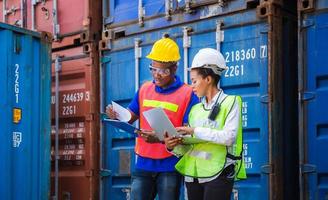 Worker man in hardhat and safety vest holding clipboard checklist and Female foreman using laptop control loading containers box from cargo photo