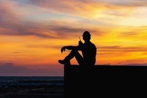 Silhouette of Foreman in hard hat sitting on container box with sunset sky photo