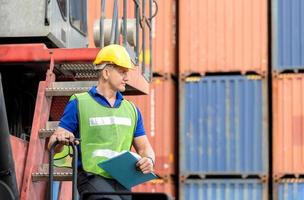 Factory worker man in hard hat and safety vest standing on container stackers control loading containers box from cargo photo