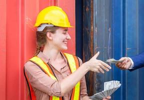 Cheerful young woman worker sitting relaxing and receiving money banknotes at container cargo photo