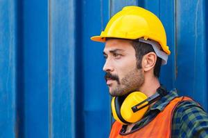 trabajador de fábrica hombre con casco y orejeras de reducción de ruido con fondo de caja de contenedores foto