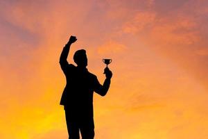 Silhouette of Business man holding award trophy show victory when business success sunset background photo