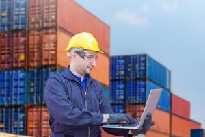 Engineer with clipping path in hardhat and safety vest holding laptop, Foreman control loading containers box from cargo photo