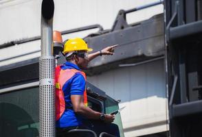 Worker man in hardhat and safety vest holding laptop standing on container stackers control loading containers box from cargo photo