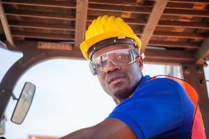 Worker man in hardhat and safety vest sitting in container stackers control loading containers box from cargo photo