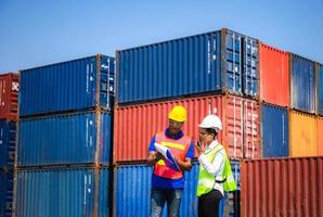 Worker man in hardhat and safety vest holding clipboard checklist and Female foreman talks on two-way radio control loading containers box from cargo photo