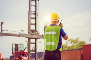 Foreman in hardhat and safety vest talks on two-way radio control loading containers box from cargo photo