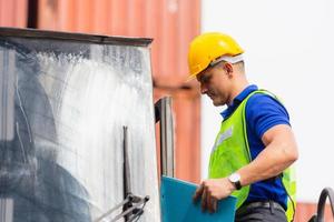 Worker man in hard hat and safety vest standing on container stackers control loading containers box from cargo photo