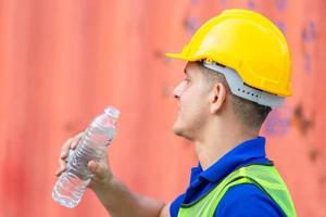 Close up of Worker man in hard hat drinking water at containers cargo photo