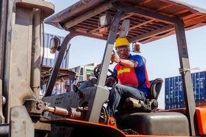 Worker man in hardhat and safety vest sitting in container stackers control loading containers box from cargo photo