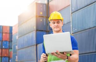 Engineer man in hardhat and safety vest holding laptop and two-way radio, Foreman worker control loading containers box from cargo photo