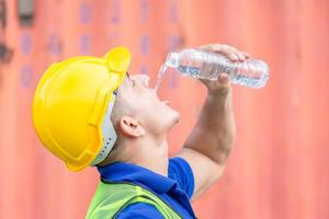 Worker man in hard hat drinking water at containers cargo photo