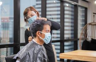 Young man getting haircut by hairdresser, Barber using scissors and comb, New normal concept photo