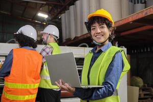 retrato de una ingeniera trabajadora con uniforme de seguridad y casco con laptop mira la cámara, sonrisa feliz y alegre, éxito en el trabajo de la industria, logro, fábrica de fabricación de técnicos profesionales. foto