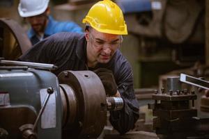 ingeniería industrial con control uniforme de seguridad que opera la máquina rectificadora de torno controlada por computadora que trabaja en la fábrica de la industria. foto